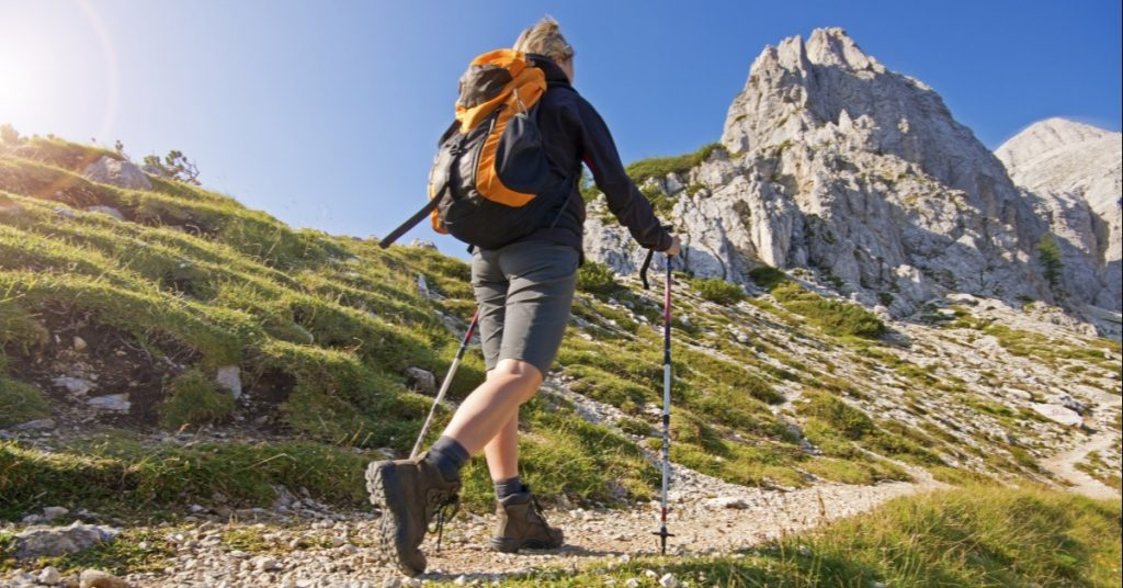 Hiker with trekking poles walking uphill toward a rocky mountain peak.
