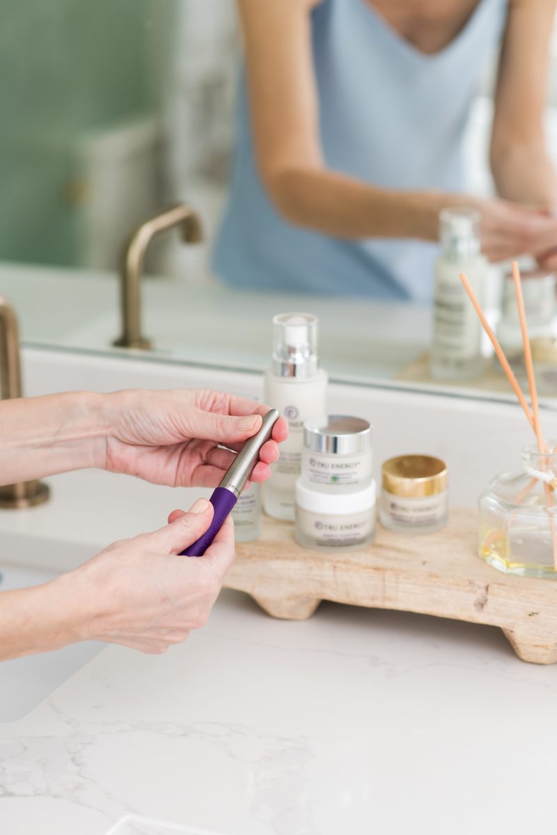 Hand choosing from a lineup of Tru Energy products and wand on a vanity